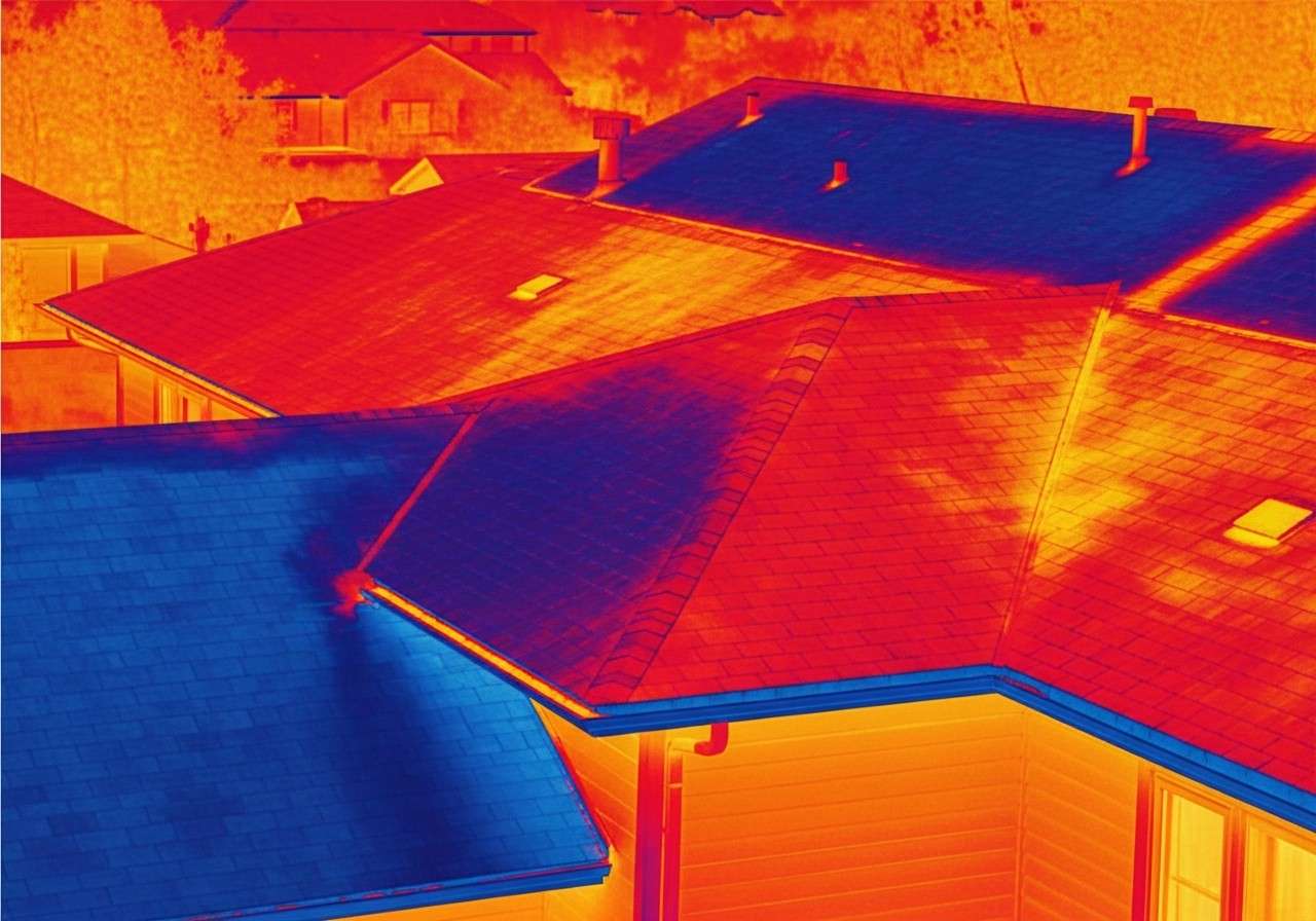 Thermal image of neighborhood rooftops showing heat distribution in red and blue hues from infrared imaging, viewed from above.